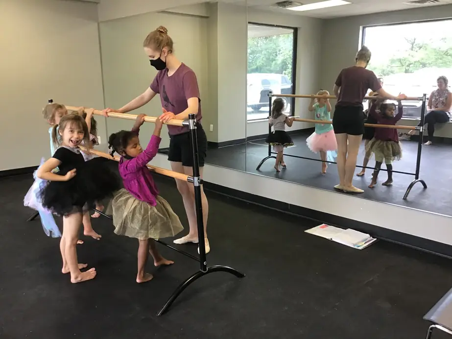 An instructor guiding young girls in tutus along a portable barre