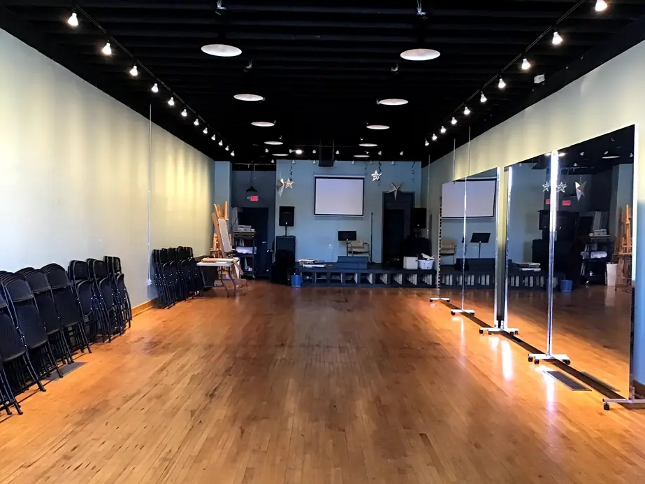 An empty studio hall with a warm wood floor, track lights and rolling mirrors