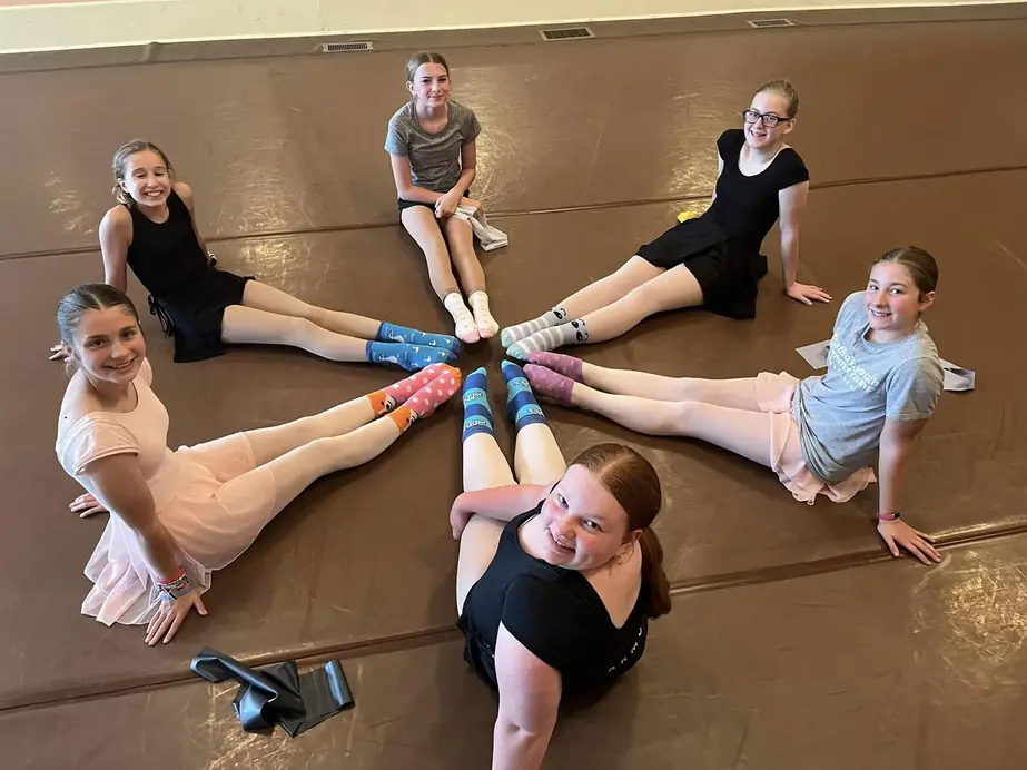 Young dancers seated on the studio floor with their feet together in a star shape