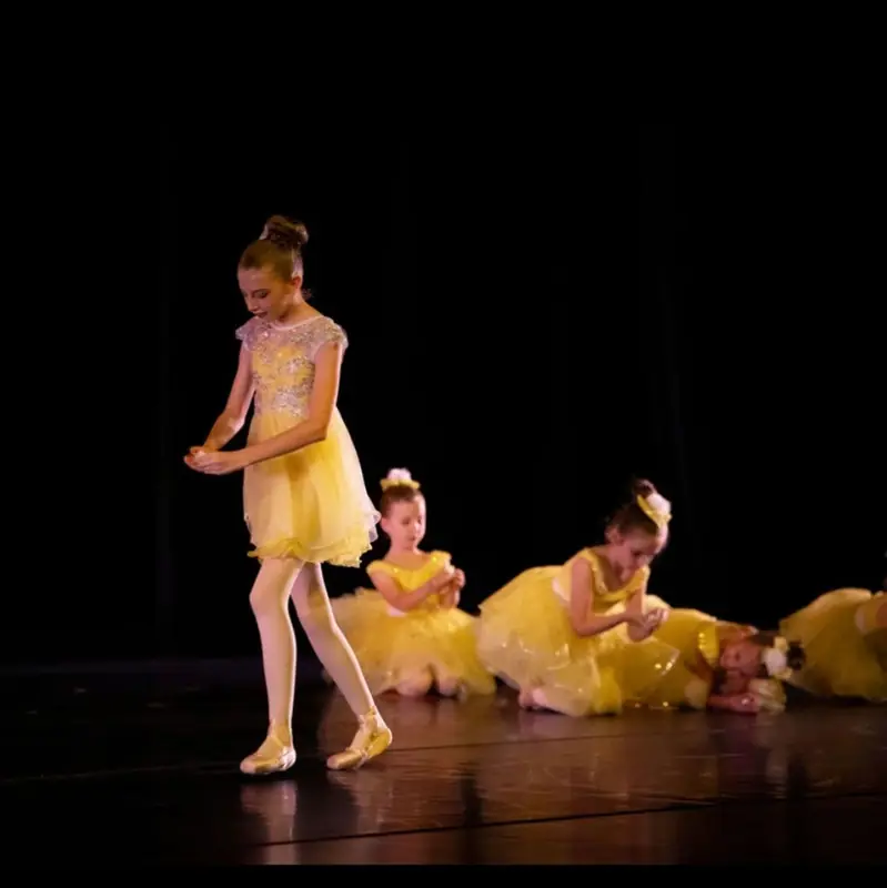 Young dancers in yellow tutus performing on a dark stage